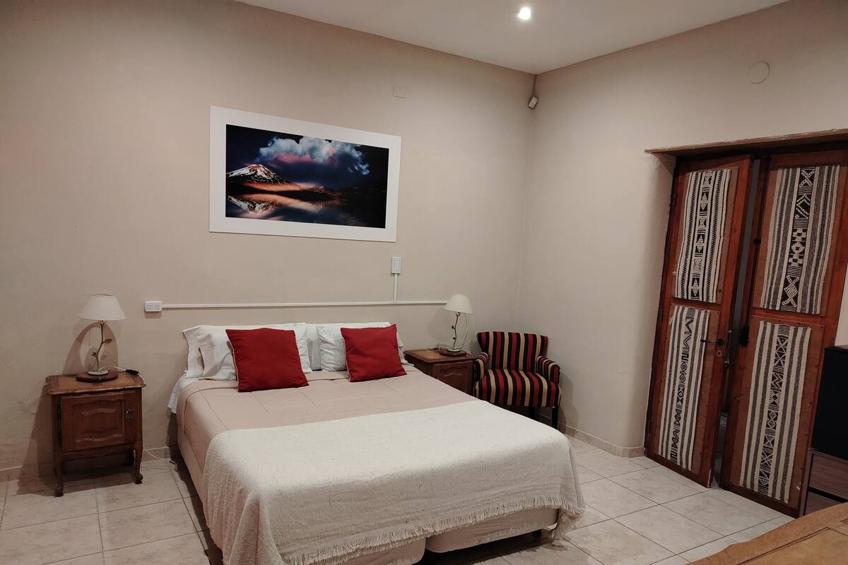 A bedroom with a bed, two bedside tables, a chair, a wardrobe, and a painting on the wall.