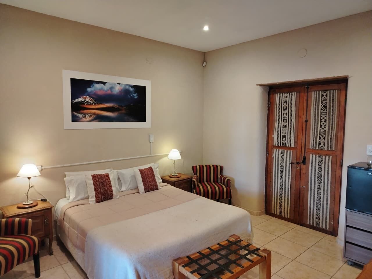 A bedroom with a bed, two bedside tables with lamps, a chair, a wardrobe, and a desk with a computer.
