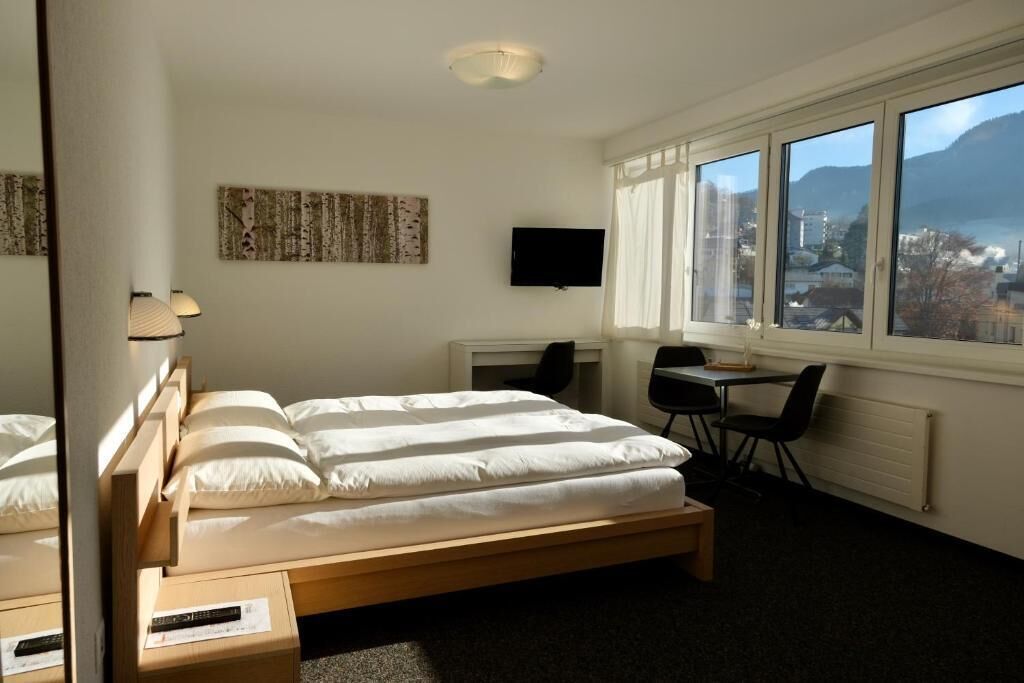 A hotel room with a bed, desk, chair, TV, and a view of the city.