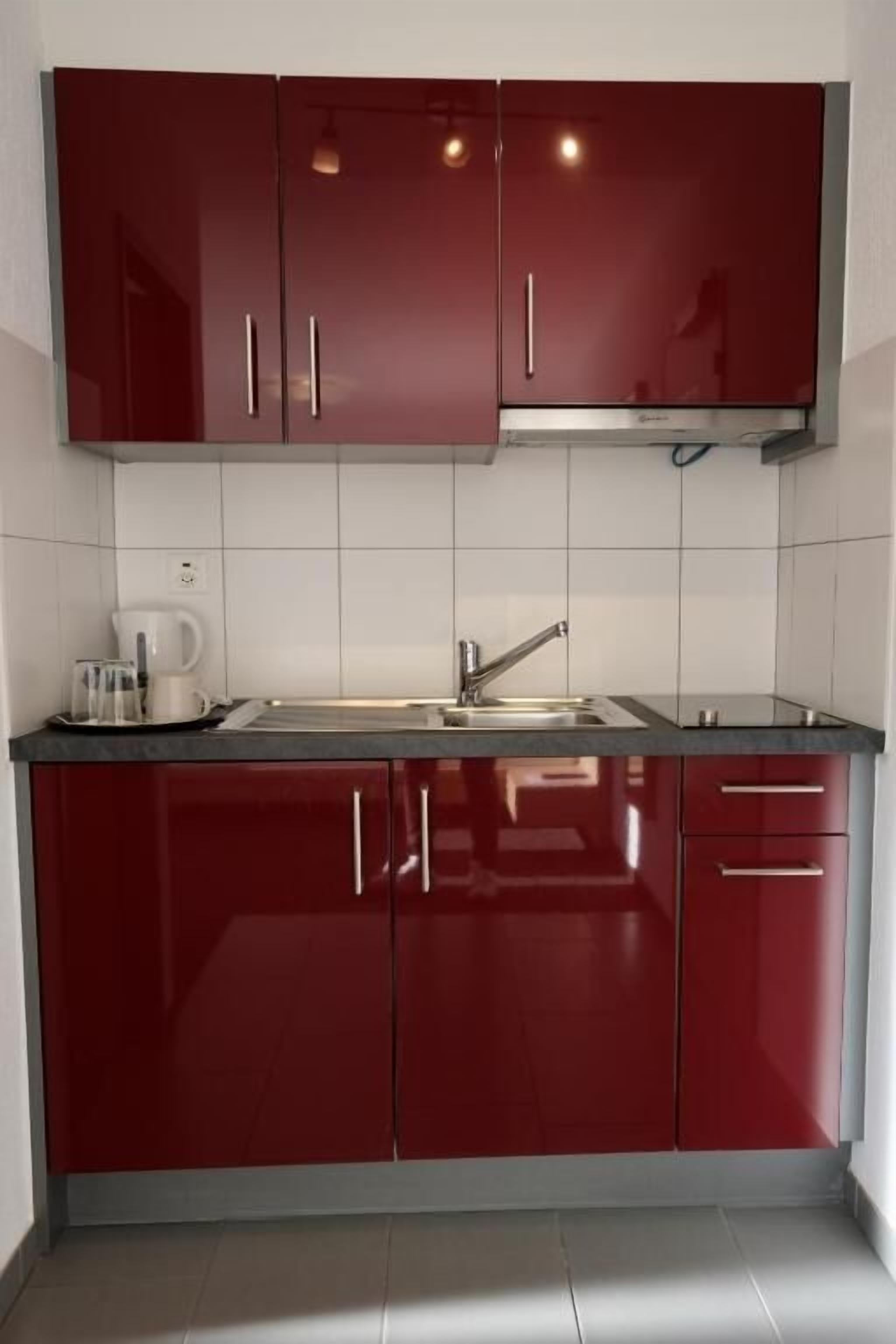 A kitchen with red cabinets, a stainless steel sink, and a coffee maker.
