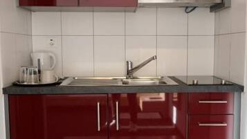 A kitchen with red cabinets, a stainless steel sink, and a coffee maker.