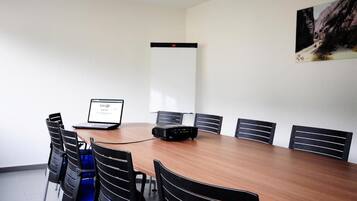A conference room with a long table, six chairs, a laptop, a projector, and a whiteboard.