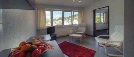 A modern living room with a dining area, large windows, and a red rug.
