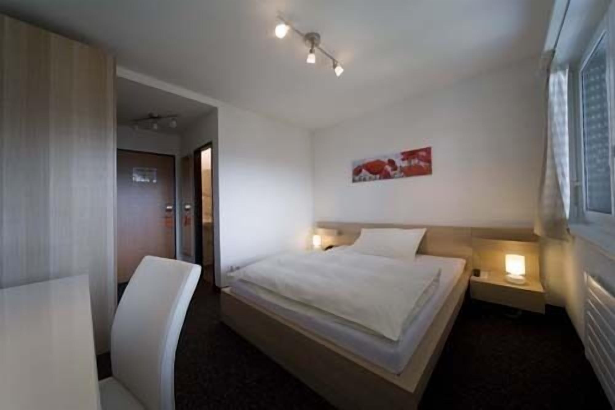 Une chambre d’hôtel avec un lit, des tables de chevet, une chaise, un luminaire au plafond et une fenêtre.