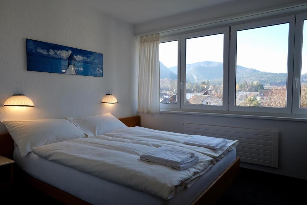 A hotel room with two beds, a painting on the wall, and a window with a view of the countryside.