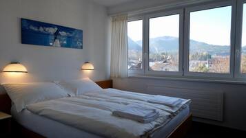 A hotel room with two beds, a painting on the wall, and a window with a view of the countryside.