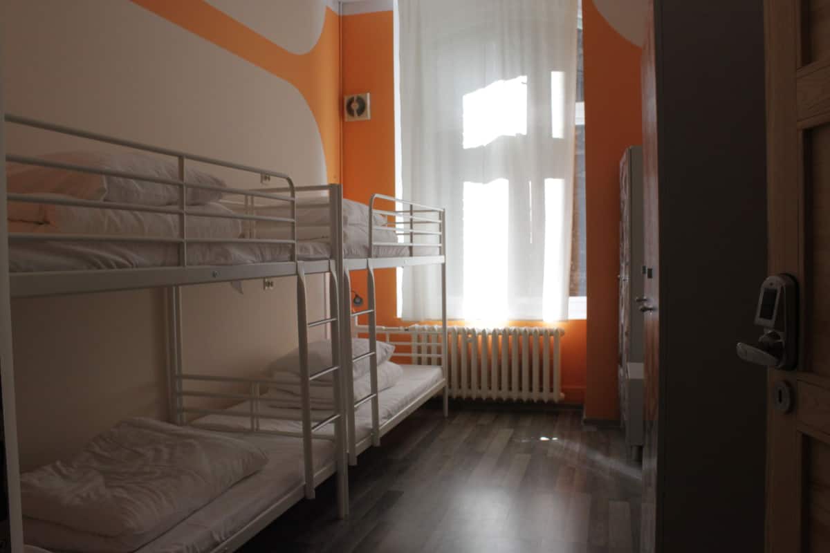 A bunk bed room with a radiator, a window with curtains, and a door.