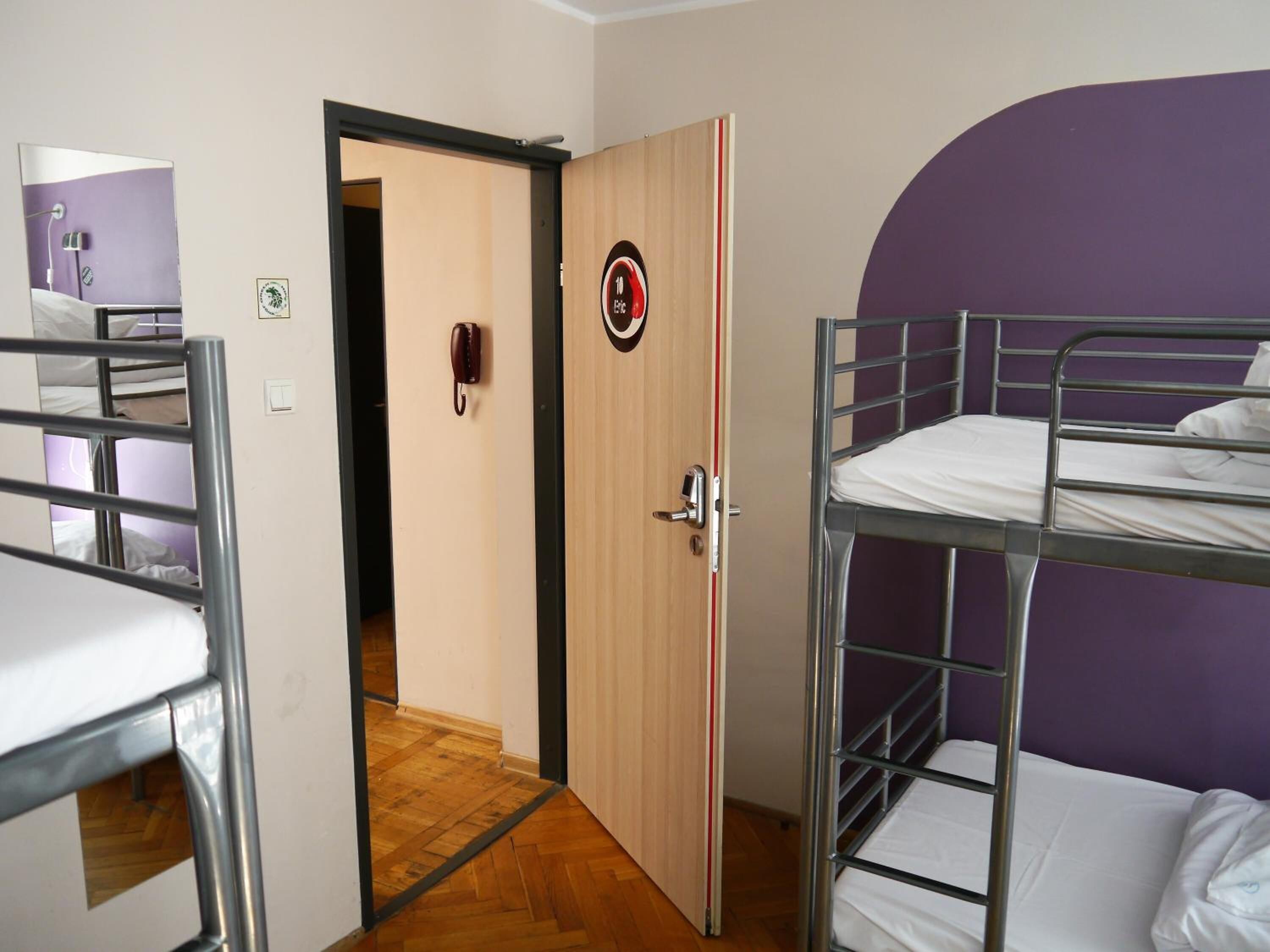 A dormitory room with bunk beds, a wooden door with a circular emblem, and a purple wall.
