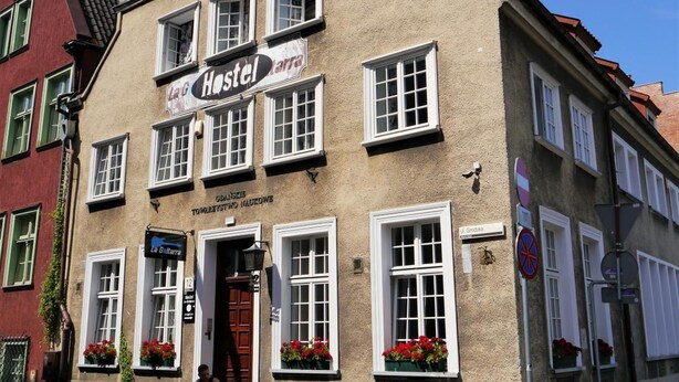 A hostel with a sign reading "Hostel Inn". It features a traditional European architectural style with multiple windows and a red door. - La Guitarra Hostel (Gdansk)