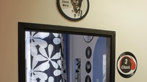 A room with a bed, a desk, and a chair. There are wall decorations including a framed picture and a circular sign with the number 3 and the name 'Chuck'. - La Guitarra Hostel (Gdansk)