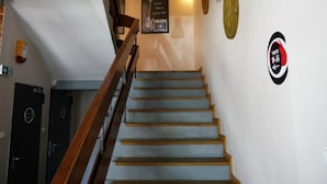 A staircase with wooden handrails leading to a landing. There are doors on the left, a sign on the wall, and a circular logo on the right. - La Guitarra Hostel (Gdansk)