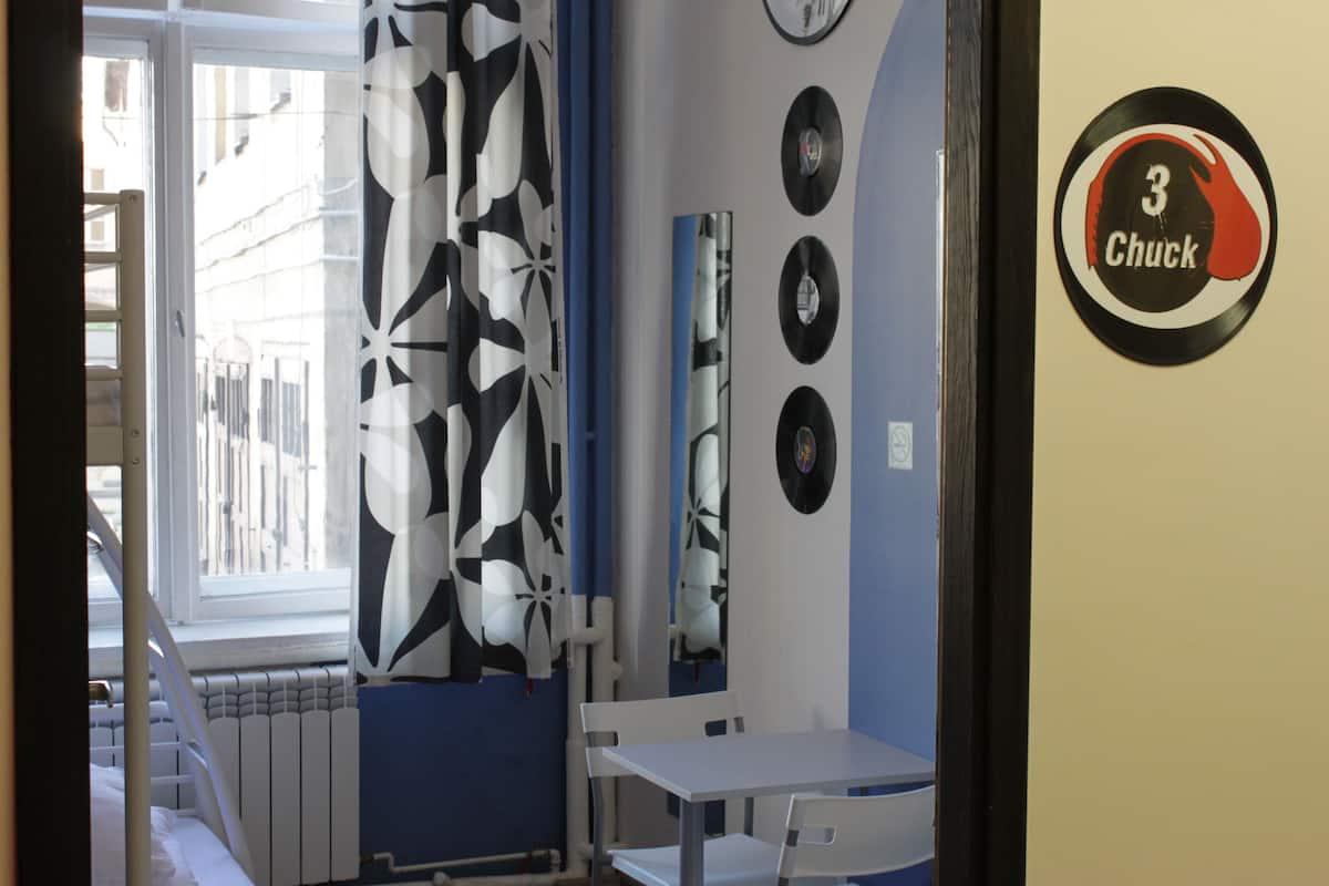 A room with a window, a radiator, a white table, and a wall with vinyl records and a '3 Chuck' sign.