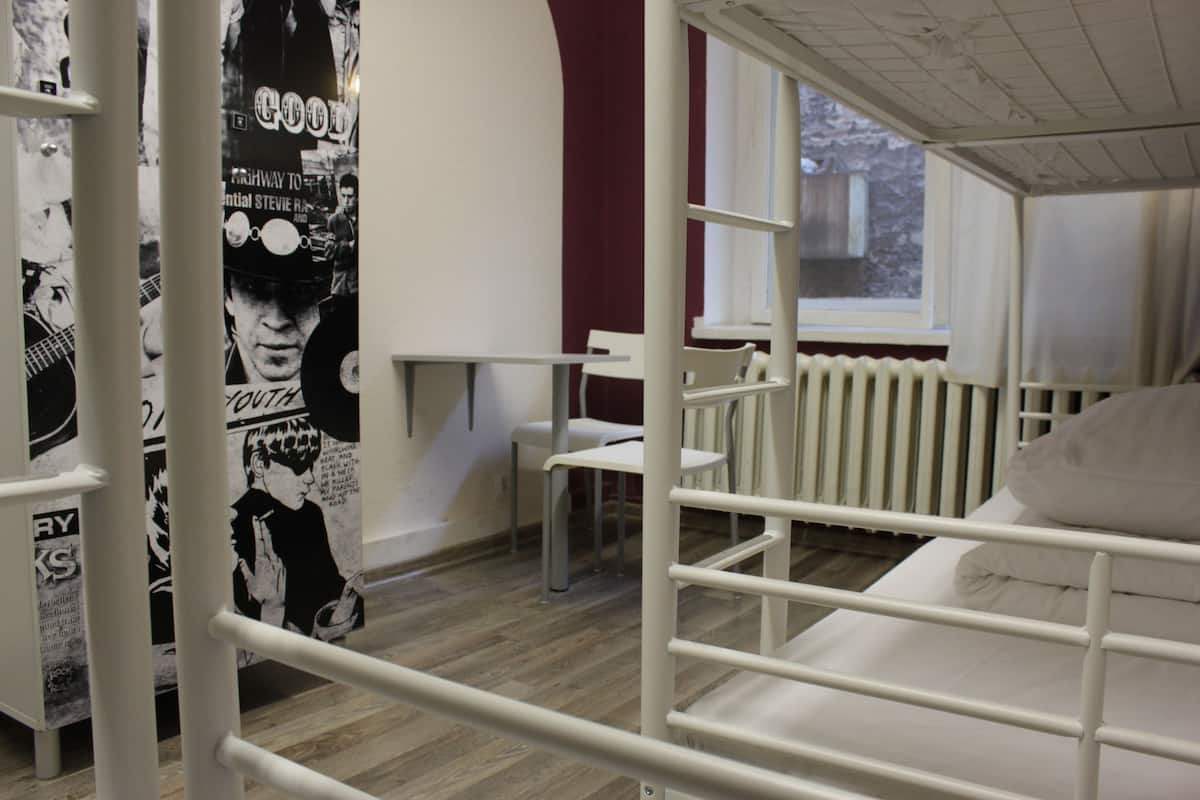 A bunk bed room with a poster on the wall, a window, and a radiator.