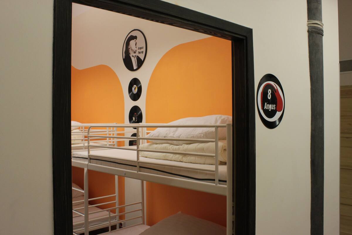 A bunk bed room with orange walls, a framed picture, and a door with a sign.