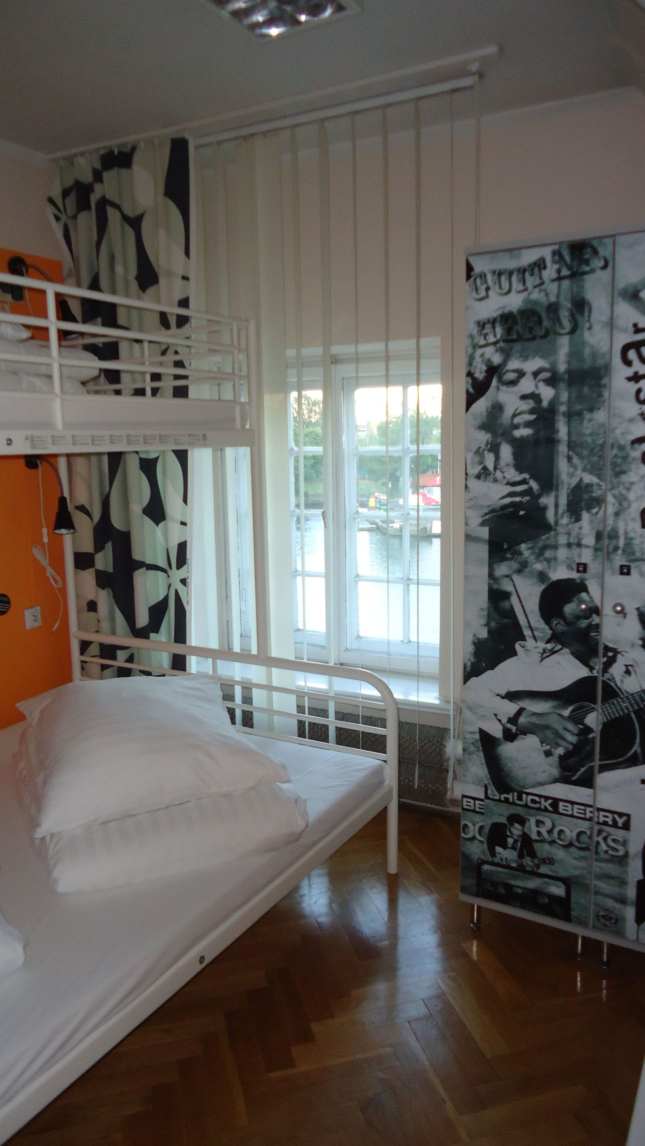 A room with bunk beds, a window with blinds, a poster on the wall, and a wooden floor.