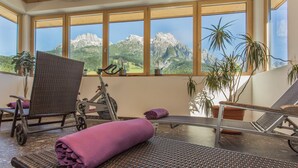 Une pièce avec vue sur les montagnes, grâce à de grandes fenêtres, meublée de meubles en osier et agrémentée de plantes en pot.