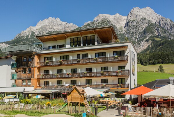 Ett hotell med flera våningar, balkonger, utomhusservering och en vacker bergsutsikt.