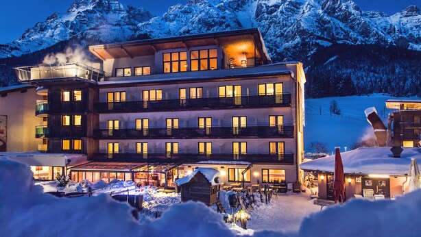 Un hôtel à plusieurs étages doté de balcons, avec une piste de ski en arrière-plan et un paysage enneigé.