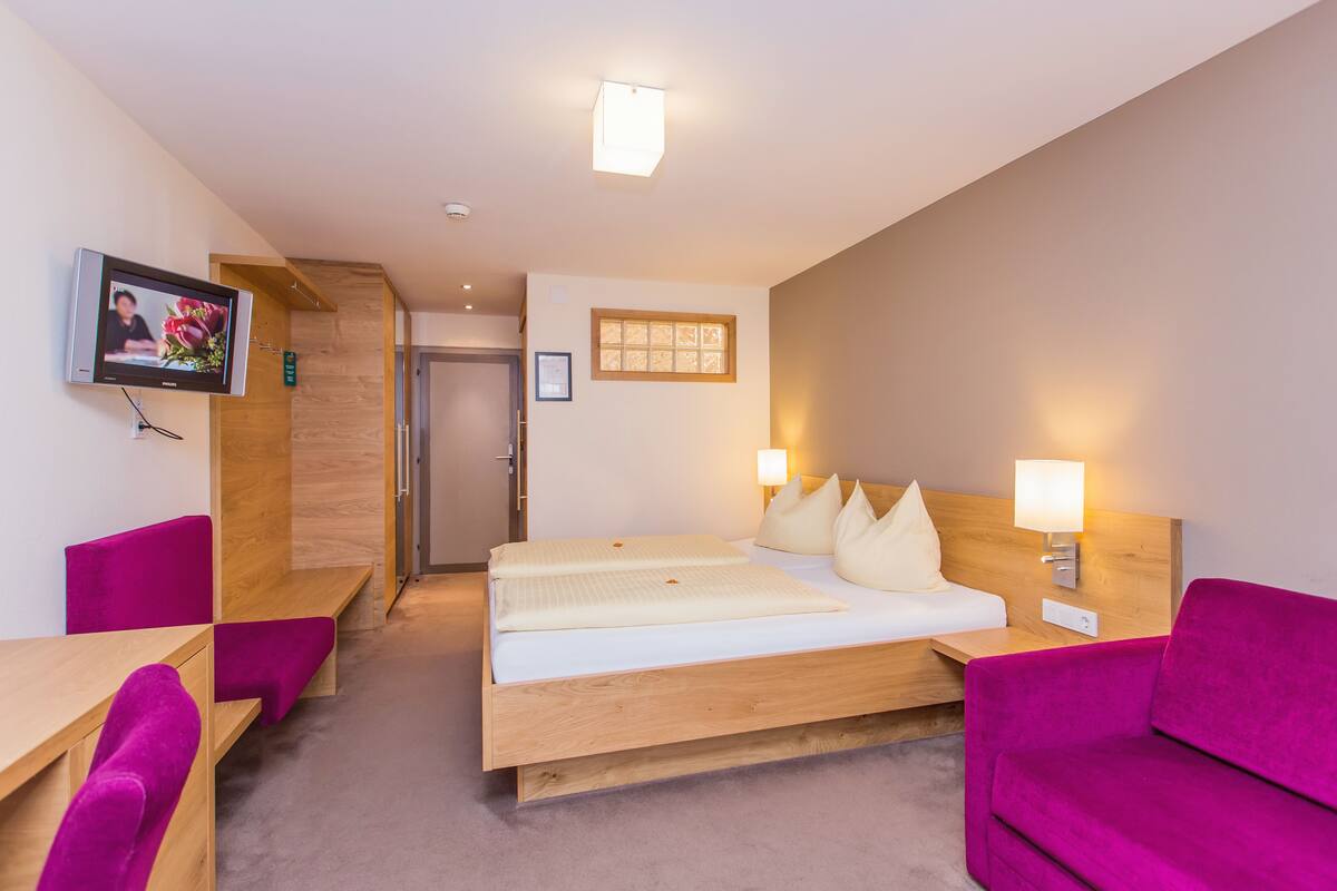 Una habitación de hotel con una cama, un escritorio, una silla, un sofá y un televisor.