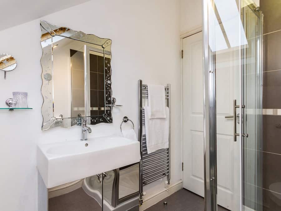 Un baño con lavamanos blanco, un espejo grande, cabina de ducha de vidrio y un perchero para toallas.