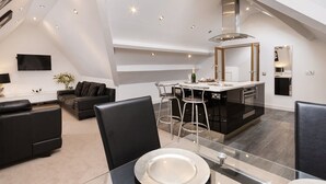 A modern kitchen with a central island, bar stools, and a dining area with a glass table and chairs. - Lincoln House Hotel (Cardiff)