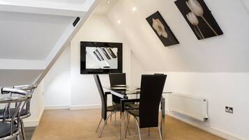 Un comedor moderno con una mesa de vidrio y sillas negras, techo blanco y obras de arte en las paredes.