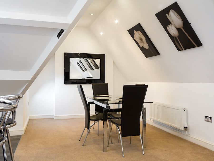 A modern dining area with a glass table and black chairs, a white ceiling, and artwork on the walls.