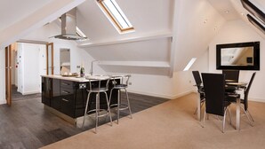 A modern kitchen with a central island, bar stools, and a dining area with chairs. - Lincoln House Hotel (Cardiff)