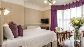 A hotel room with a large bed, a television, a dining table, and a vase with flowers.