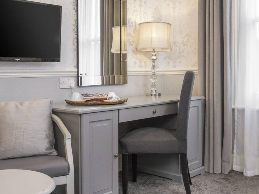 Habitación de hotel con un escritorio gris, una silla, un televisor, una lámpara y un espejo grande.