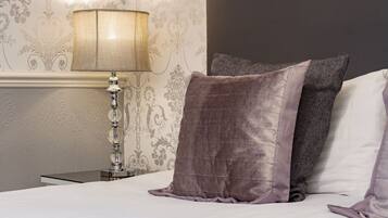 A neatly made bed with a white and gray pillow, a textured lamp, and a wall with floral wallpaper.