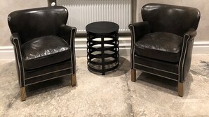 Una habitación con dos sillones de cuero, una mesita redonda y una chimenea decorada con objetos.