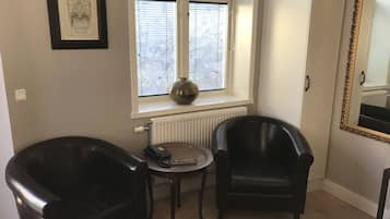 Een kamer met twee zwarte leren fauteuils, een kleine tafel met een vaas, een ingelijst schilderij aan de muur en een grote spiegel.