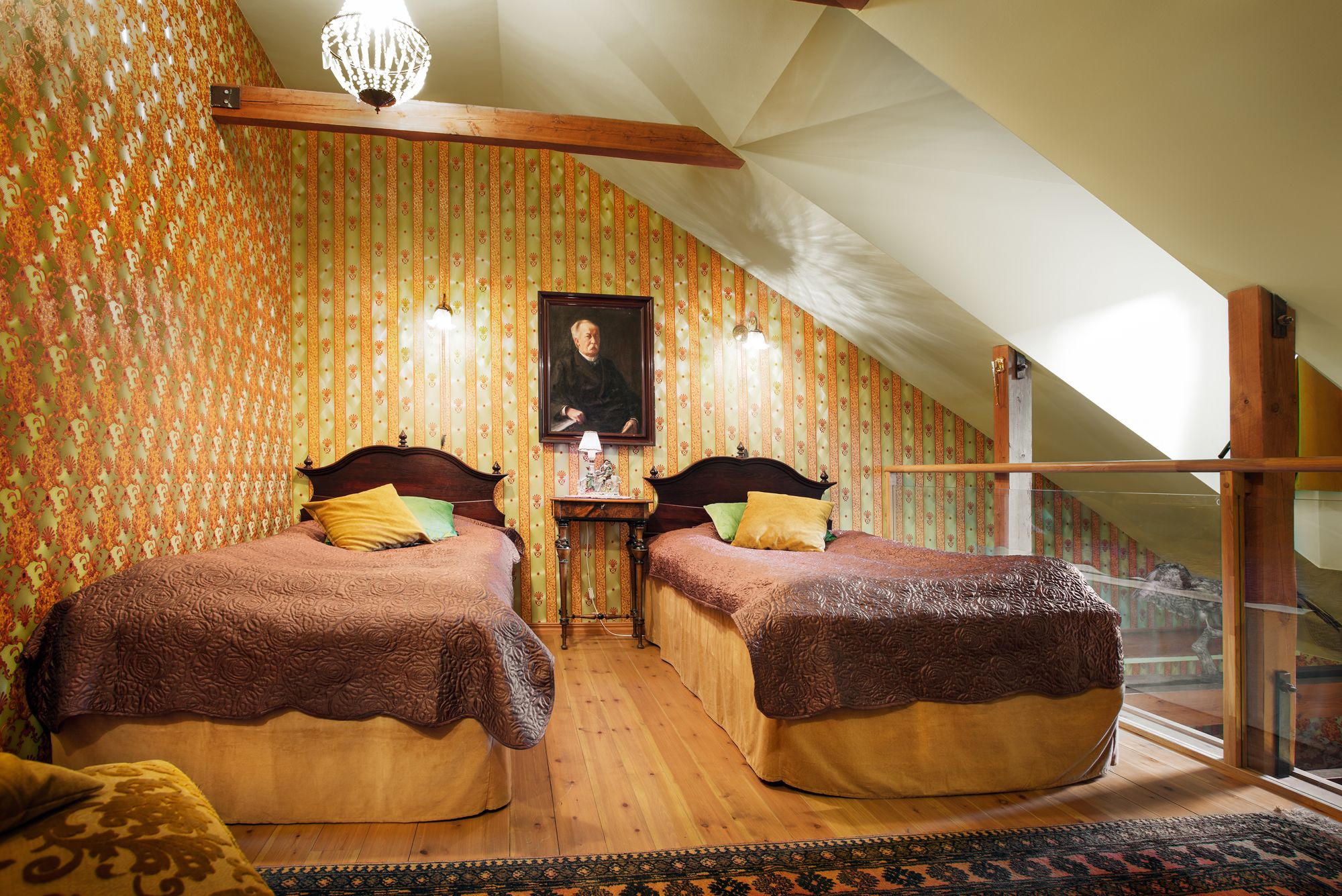 A bedroom with two beds, patterned wallpaper, a chandelier, and a painting on the wall.