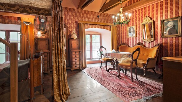 Una habitación con una escalera de madera, una mesa de comedor con sillas, un tapete rojo estampado y un espejo grande en la pared.