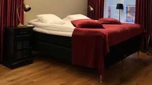 Un dormitorio con una cama, una mesita de noche, una lámpara y un ventanal con cortinas.
