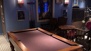 Una mesa de billar en una habitación con paredes azules, piso a cuadros y obras de arte enmarcadas.