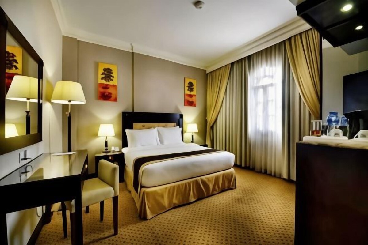 A hotel room with a bed, desk, chair, and a television.