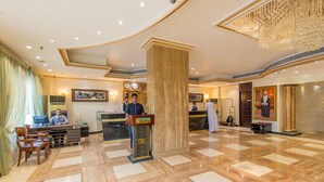 A hotel lobby with a reception desk, a large column, and a chandelier. -  Caesar Hotel (Muscat)