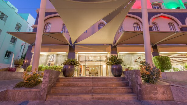 A hotel entrance with a grand staircase, large potted plants, and a canopy structure. -  Caesar Hotel (Muscat)