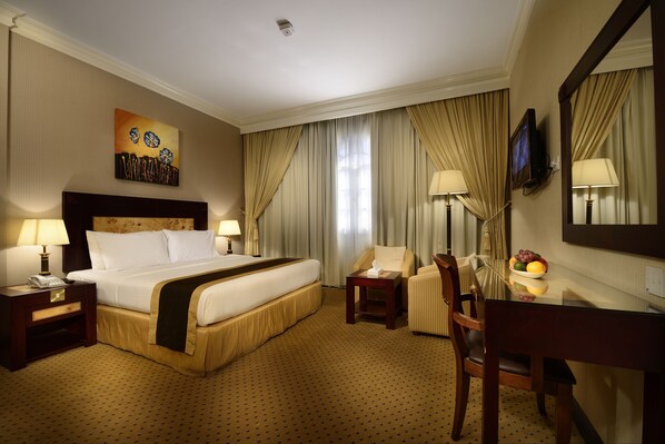 A hotel room with a large bed, a desk, a chair, a television, and a painting on the wall. - Caesar Hotel (Muscat)