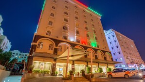 A multi-story hotel with a prominent entrance, outdoor seating area, and a well-lit facade. -  Caesar Hotel (Muscat)