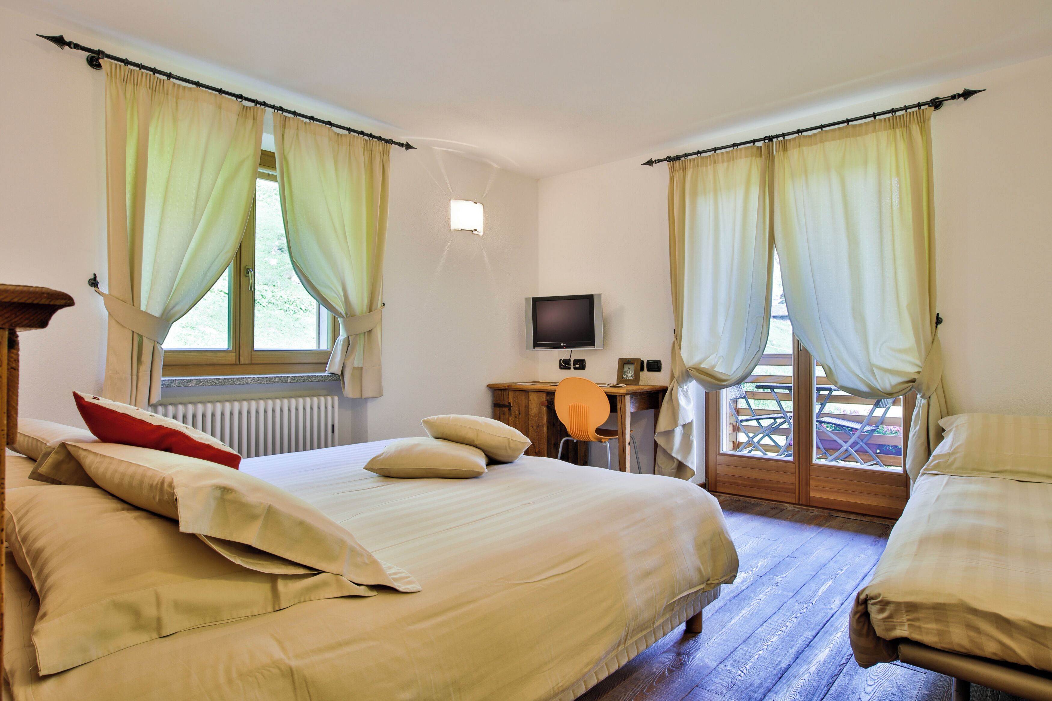Un dormitorio con cama, escritorio, televisor y vistas al exterior.