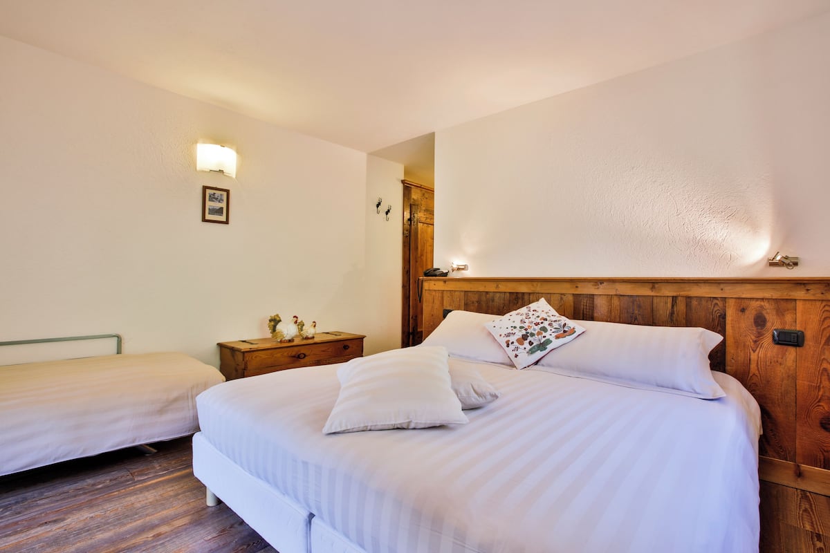 A bedroom with two single beds, a wooden headboard, a nightstand with a lamp, and a wall-mounted light fixture.