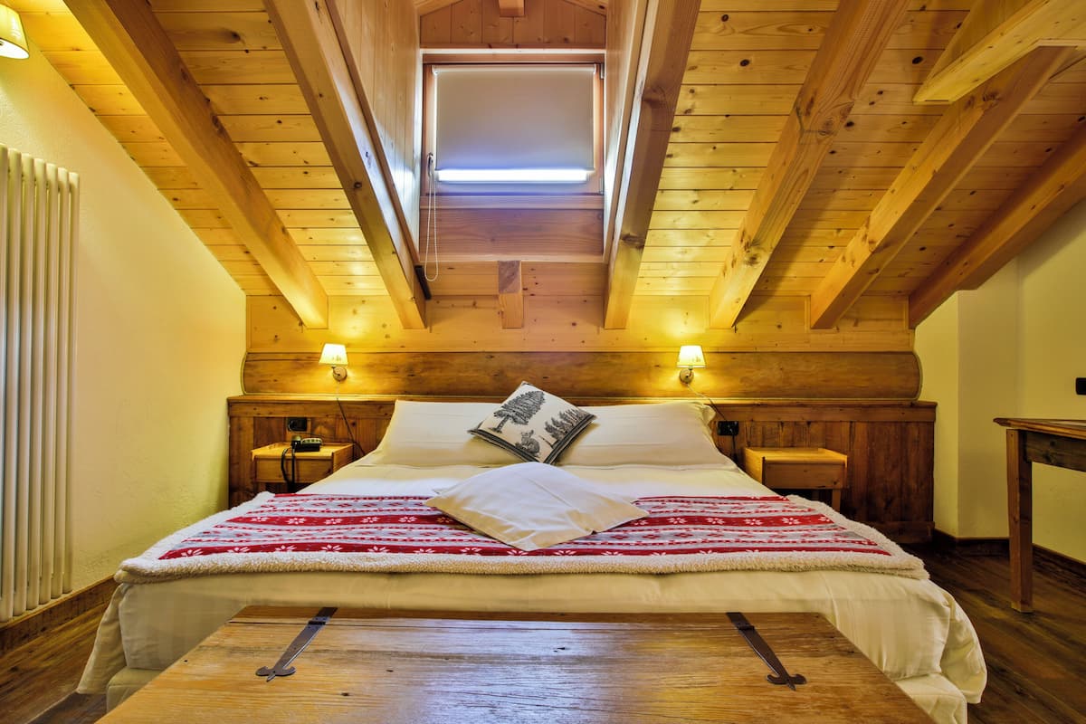 A cozy bedroom with a wooden ceiling, a skylight, a bed with a red and white blanket, two bedside tables with lamps, and a wooden nightstand.