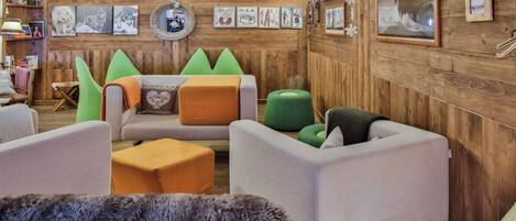 Una habitación acogedora con paredes de madera, un sofá, dos otomanas verdes y una alfombra mullida.