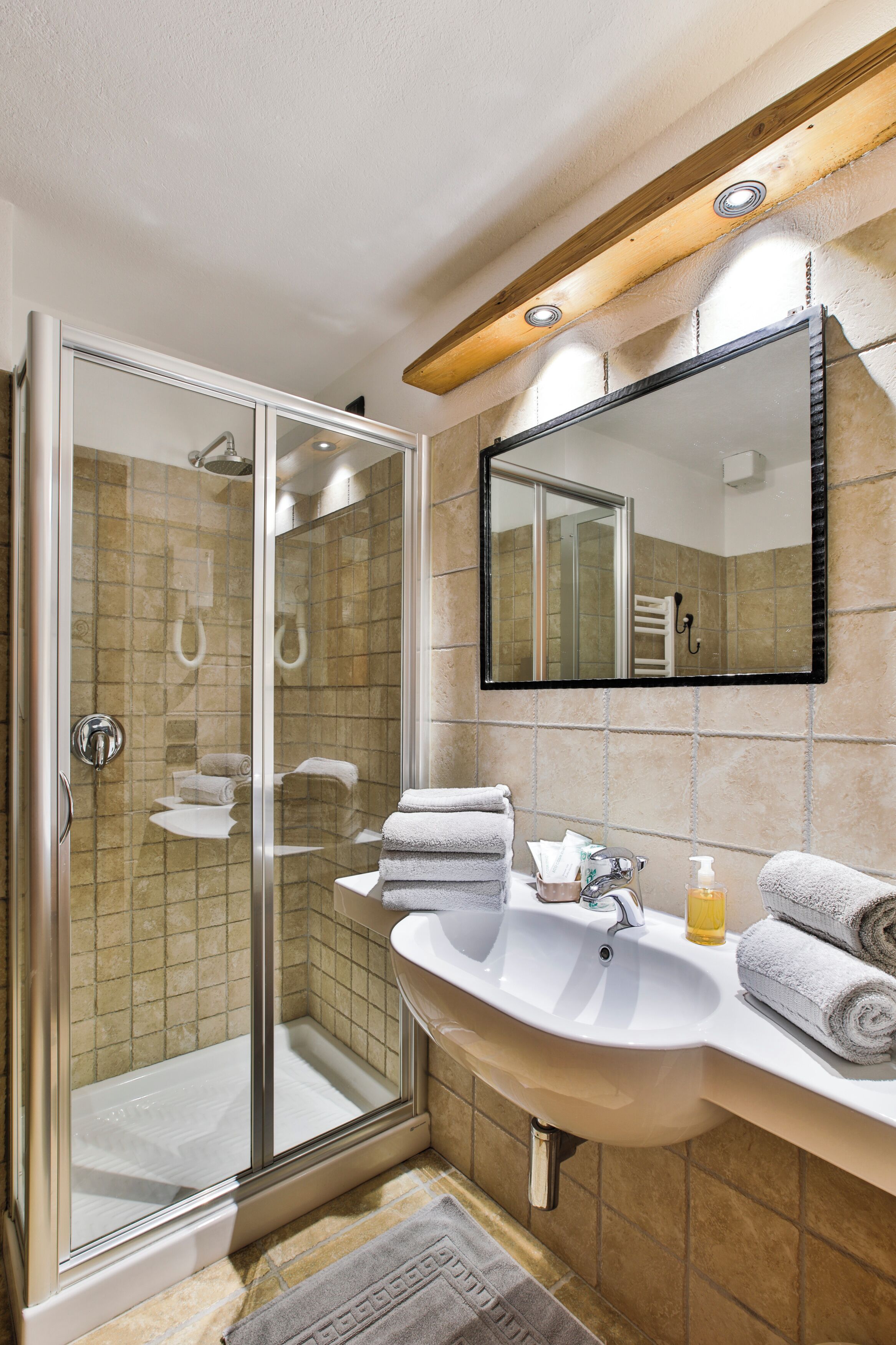 A bathroom with a glass-enclosed shower, a sink with a mirror above, and towels on the counter.