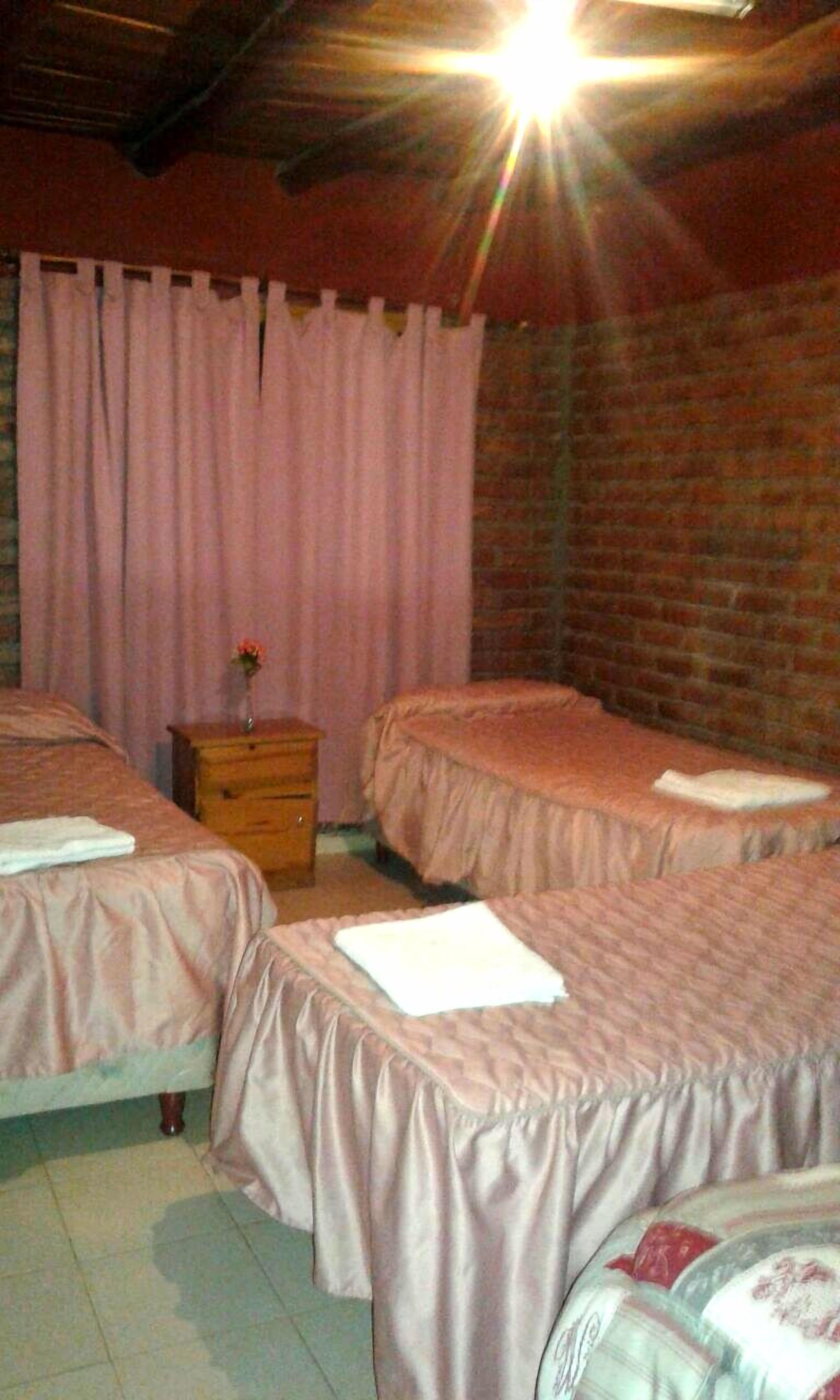 A room with two beds, a wooden nightstand, and a brick wall.