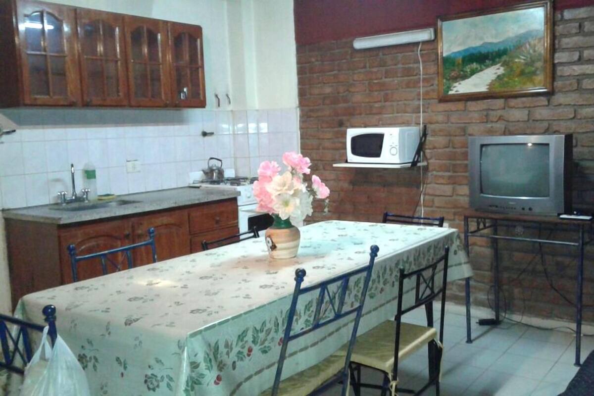 A kitchen with wooden cabinets, a microwave, a television, and a dining table with chairs.