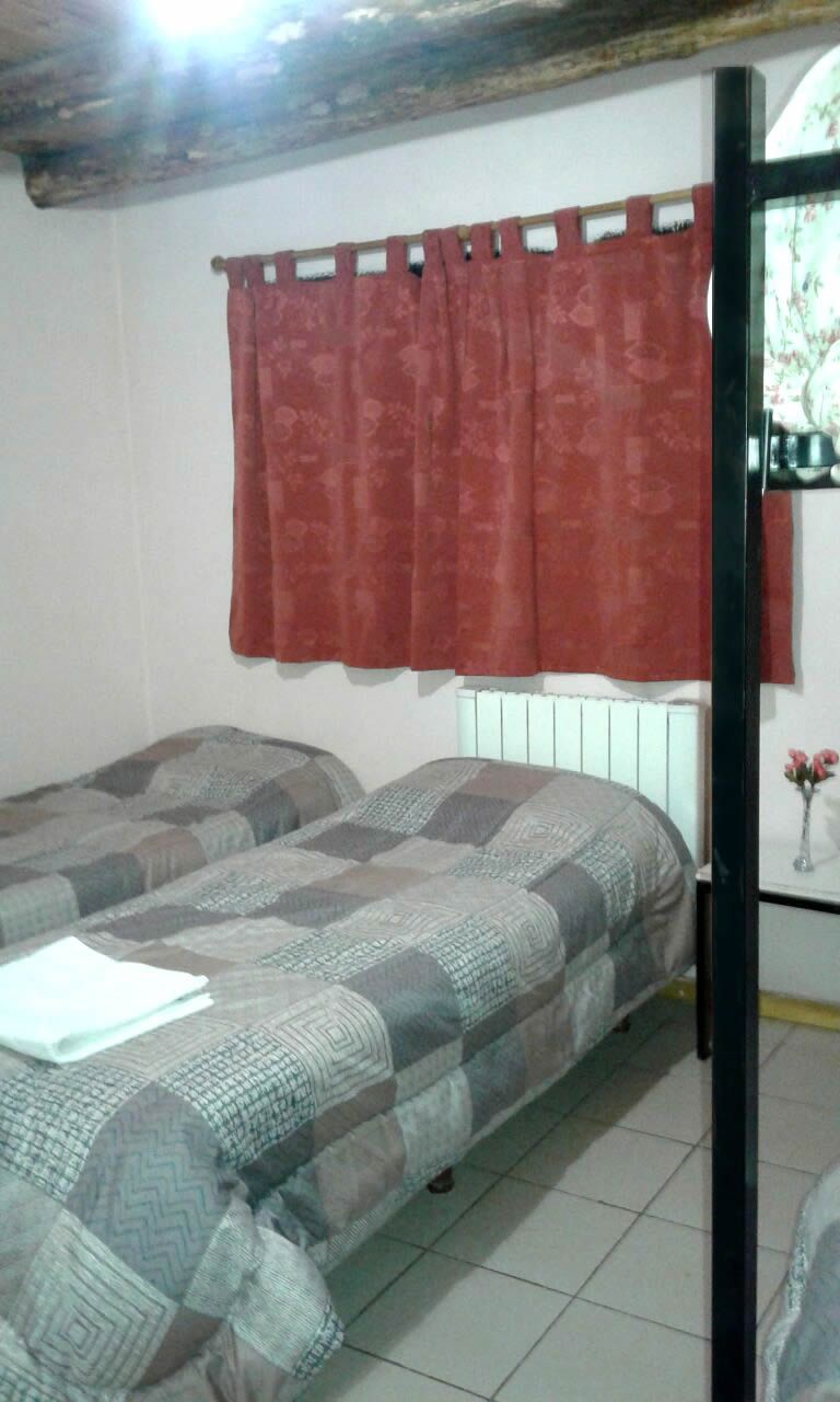 Quarto com duas camas, cortina vermelha, radiador branco e um espelho.